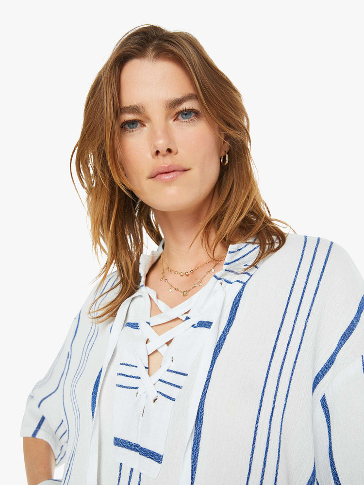 Detailed view of a woman in a white and blue striped blouse  designed with a V-neck that laces and ties, drop shoulders, elbow length sleeves and a loose, boxy fit. 