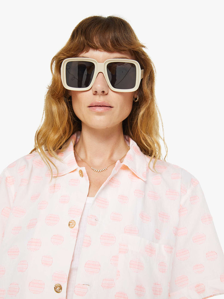 Front close up view of a woman wearing an white oversized short sleeve button down shirt with pink polka dots.