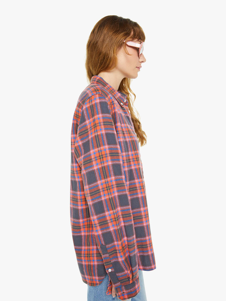 Side view of a woman long sleeve button-up shirt in a pink and navy checkered print, and is designed with a patch pocket and loose, boxy fit.