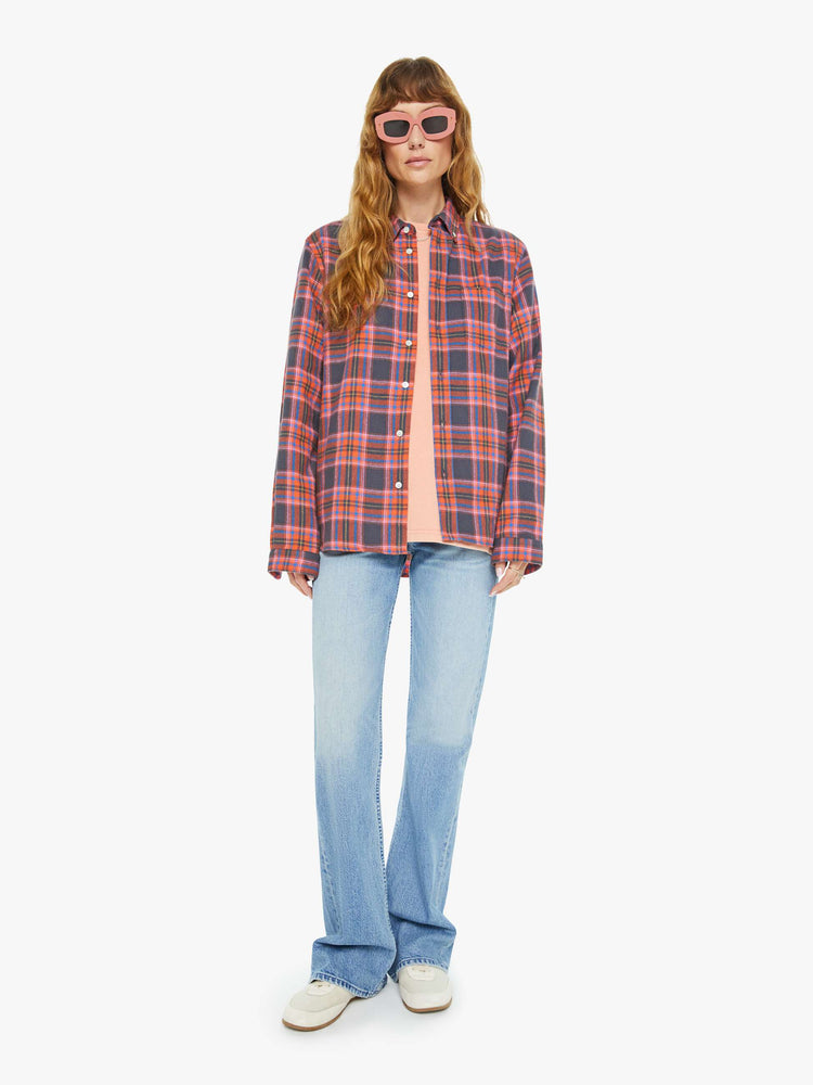 Full body view of a woman long sleeve button-up shirt in a pink and navy checkered print, and is designed with a patch pocket and loose, boxy fit.