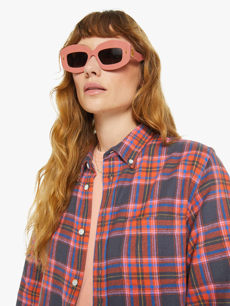 Close up view of a woman long sleeve button-up shirt in a pink and navy checkered print, and is designed with a patch pocket and loose, boxy fit.