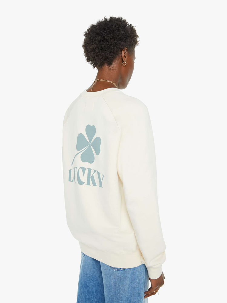 Back view of a woman in an off white sweatshirt with a relaxed shape with raglan sleeves and is decorated with a four leaf clover graphic and text on the back.