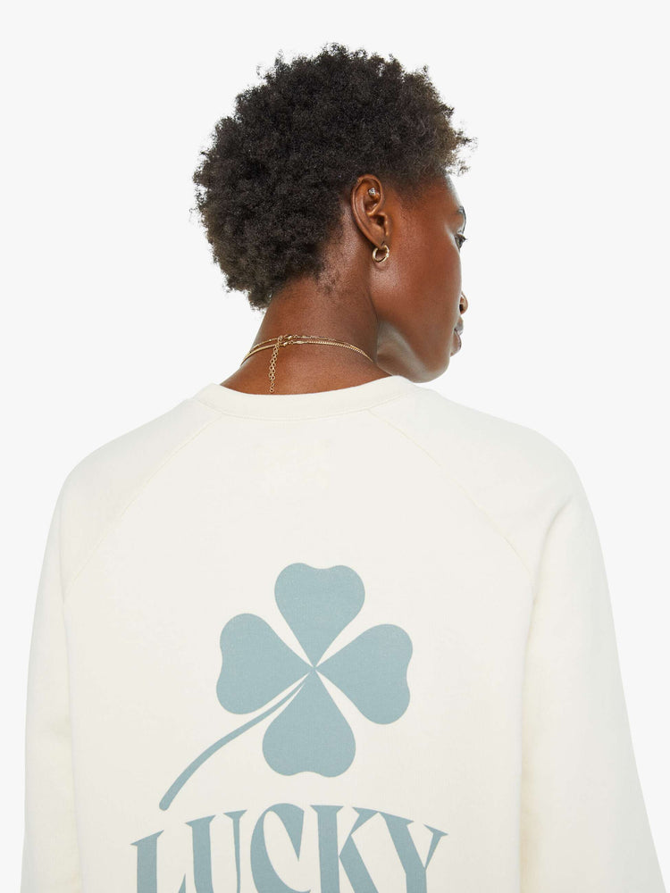 Close up back view of a woman in an off white sweatshirt with a relaxed shape with raglan sleeves and is decorated with a four leaf clover graphic and text on the back.