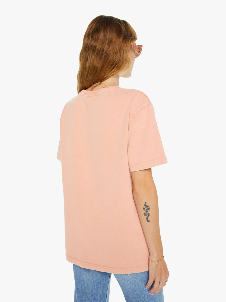 Back view of a woman light peach tee with a white anchor graphic on the chest, has a ribbed crewneck and a straight fit.