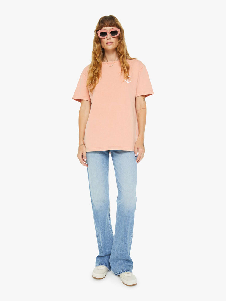 Full body view of a woman light peach tee with a white anchor graphic on the chest, has a ribbed crewneck and a straight fit.