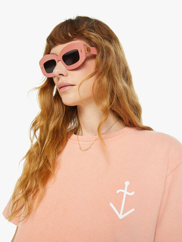 Close up view of a woman light peach tee with a white anchor graphic on the chest, has a ribbed crewneck and a straight fit.