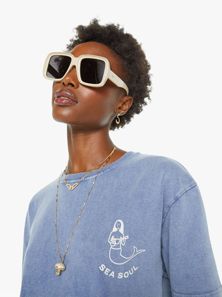 Close up view of a woman in a faded blue with a white anchor graphic on the chest, has a ribbed crewneck and a straight fit.