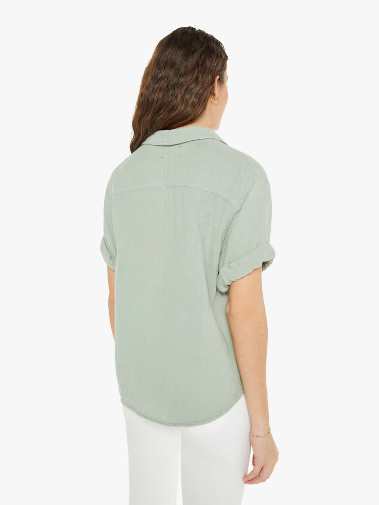 Back view of a woman in a collared blouse with a V-neck, rolled short sleeves, a curved hem and loose fit in a soft grey.