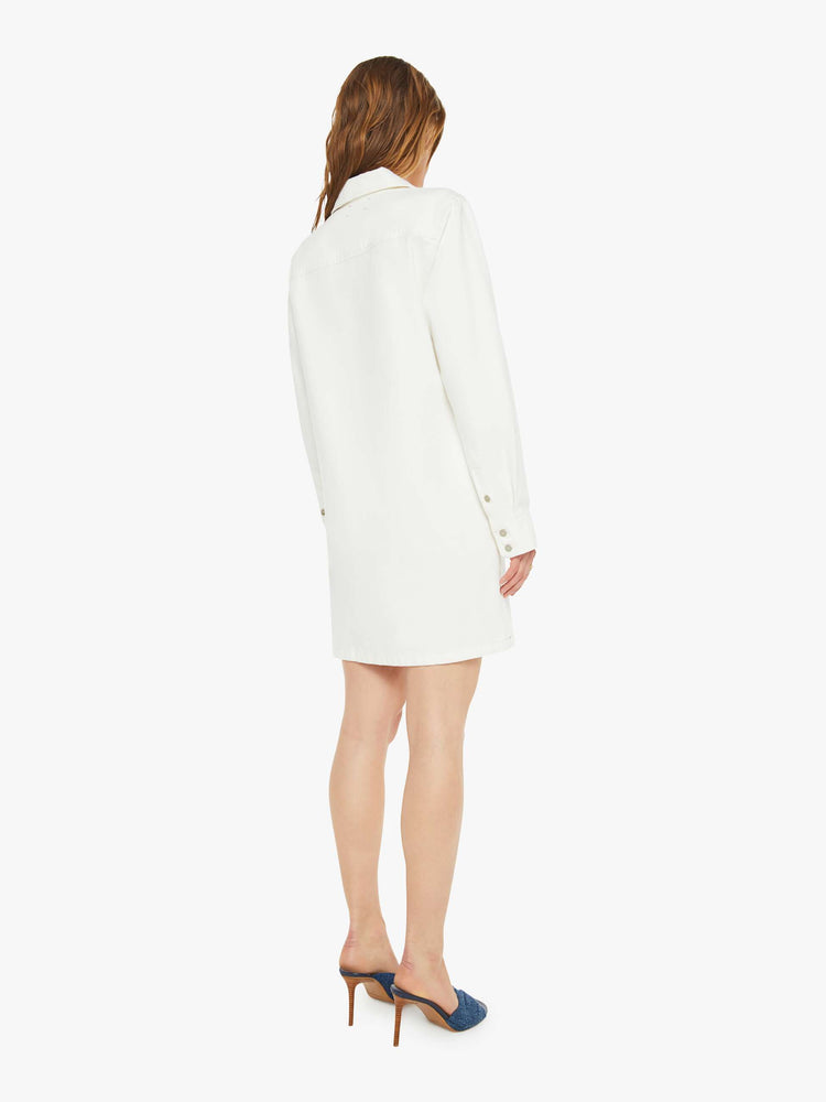 Back view of a woman in a white mini dress with a collared V-neck, long sleeves, a front patch pocket and a boxy fit.