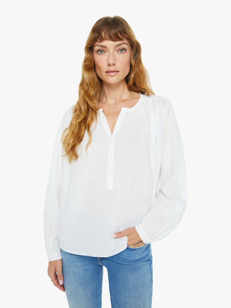 Front view of a woman white long sleeve  buttoned V-neck, long balloon sleeves and has a loose, flowy fit.