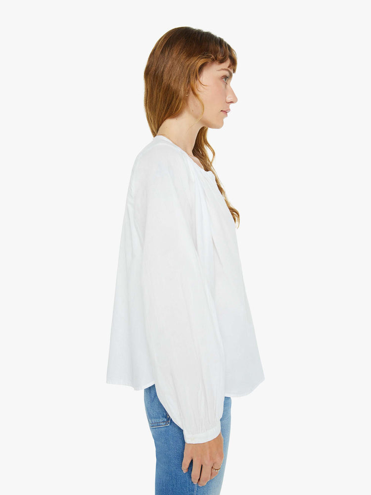 Side view of a woman white long sleeve buttoned V-neck, long balloon sleeves and has a loose, flowy fit.