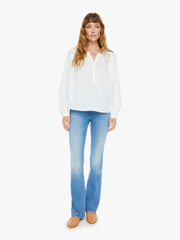 Full body view of a woman white long sleeve buttoned V-neck, long balloon sleeves and has a loose, flowy fit.