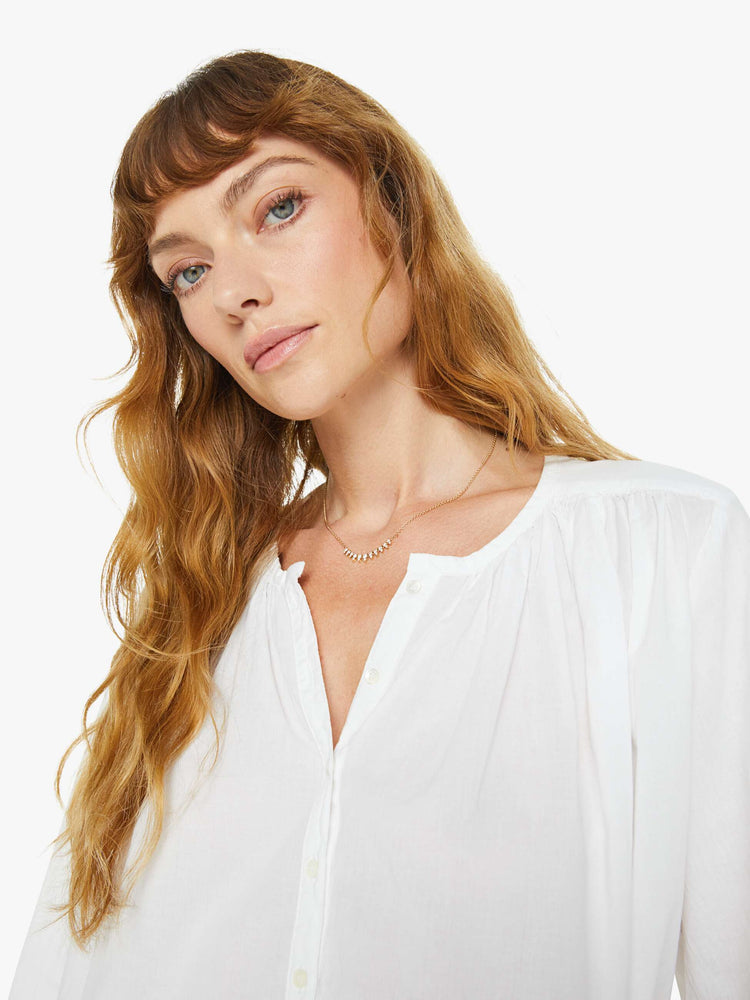 Close up view of a woman white long sleeve buttoned V-neck, long balloon sleeves and has a loose, flowy fit.