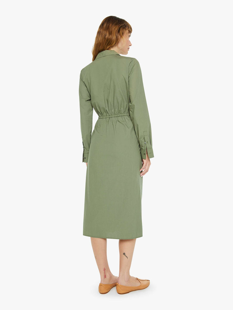 Back view of a woman in an army green dress with a collared V-neck that buttons, a gathered, tied waistband and a calf-grazing hem.