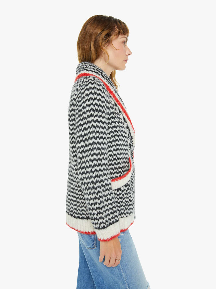 Side view of a woman in a black and cream stripes with red trim sweater with a shawl collar, deep V-neck, slit pockets, ribbed hems and a slightly oversized fit.