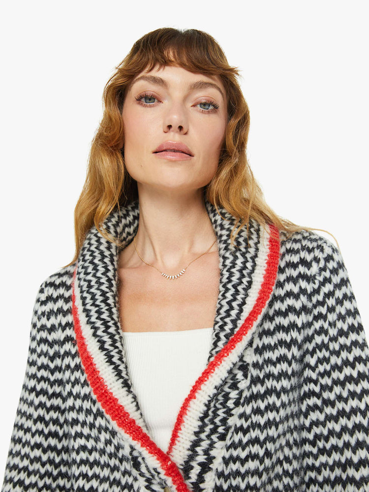 Close up view of a woman in a black and cream stripes with red trim sweater with a shawl collar, deep V-neck, slit pockets, ribbed hems and a slightly oversized fit.