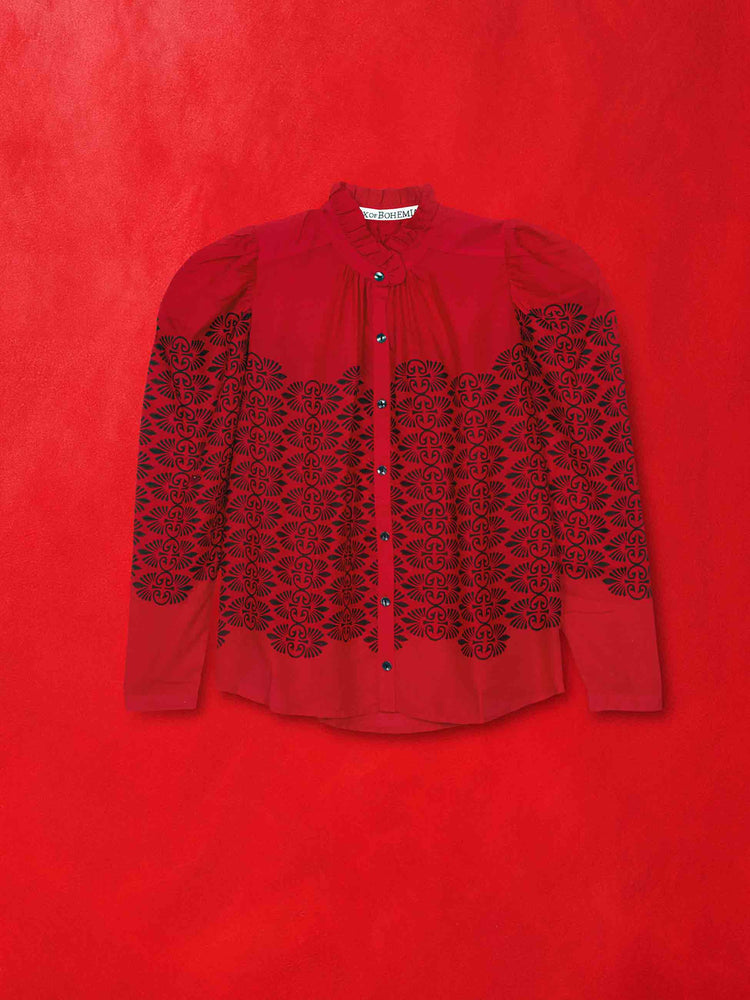 Flat view of a red blouse with a black floral patten, against a red background.