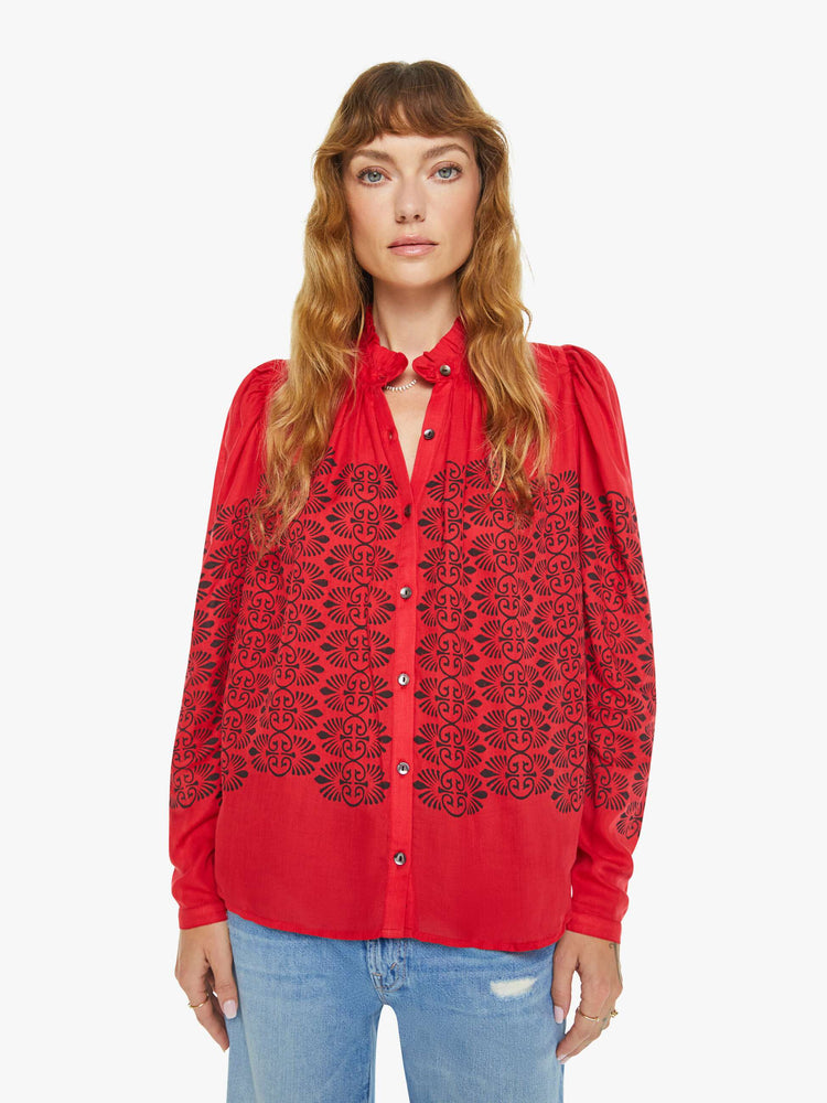 Front view of a woman blouse in red with black printed details, and features a ruffled collar, puffed shoulders, buttons down the front and a slightly cropped fit.