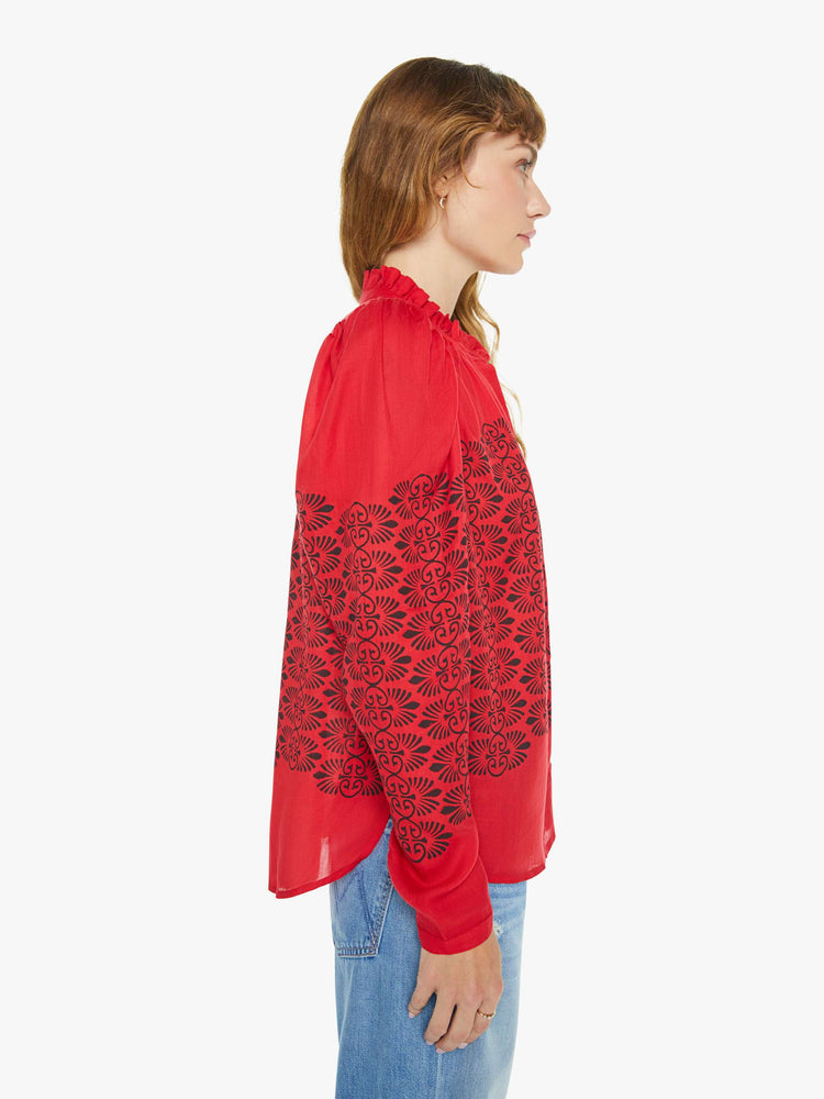 Side view of a woman blouse in red with black printed details, and features a ruffled collar, puffed shoulders, buttons down the front and a slightly cropped fit.