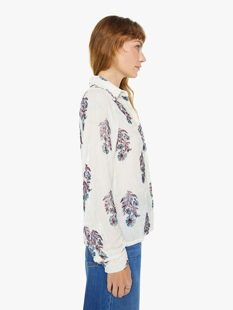 Side view of a woman blouse in off-white velvet with a cool-toned floral print, and features a collared neck, buttons down the front and long sleeves.