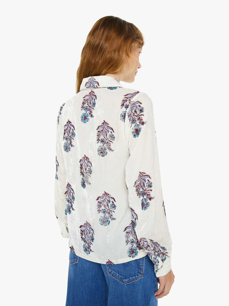 Back view of a woman blouse in off-white velvet with a cool-toned floral print, and features a collared neck, buttons down the front and long sleeves.