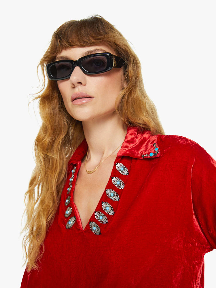 Close up view of a woman blouse in red velvet with embellishments at the neck, and features a collared V-neck, drop shoulders, long sleeves and a loose fit.