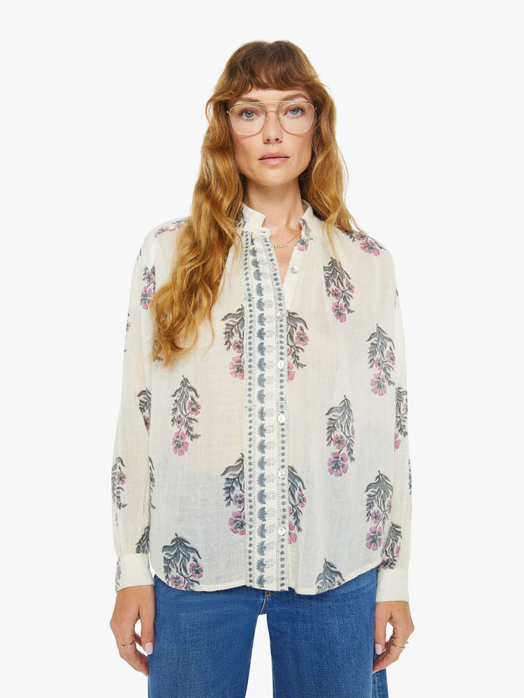 Front view of a woman blouse in cream with a grey and pink floral print, and features a stacked collar, buttoned V-neck, long sleeves and a loose fit.