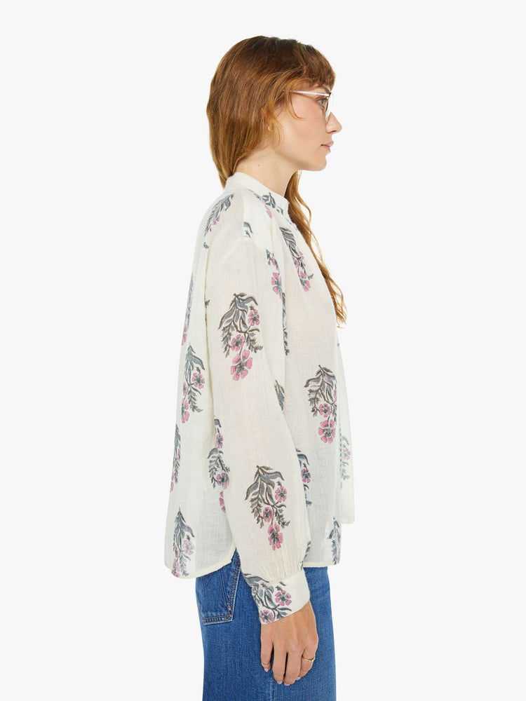 Side view of a woman blouse in cream with a grey and pink floral print, and features a stacked collar, buttoned V-neck, long sleeves and a loose fit.