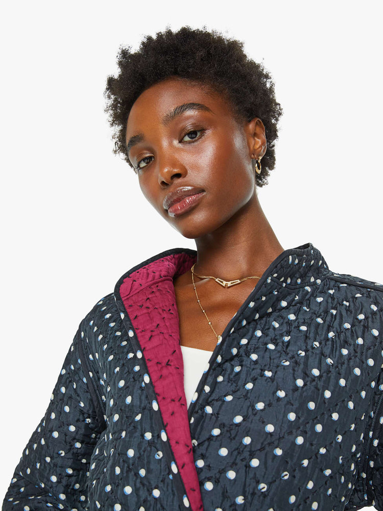 Close up front view of a woman jacket  in navy with white polka dots and red trim, and features a V-neck, front patch pockets and a tied waist.