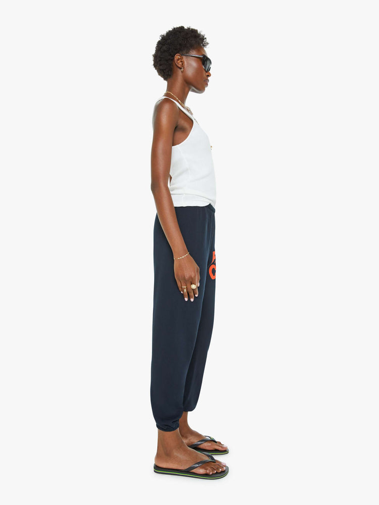 Side view of a woman in a navy color sweatpants with a drawstring waistband, elastic hems, a loose, wide leg and the brand's logo in grey at the hip.