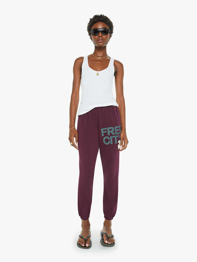 Front view of a woman in an eggplant color sweatpants with a drawstring waistband, elastic hems, a loose, wide leg and the brand's logo in grey at the hip.