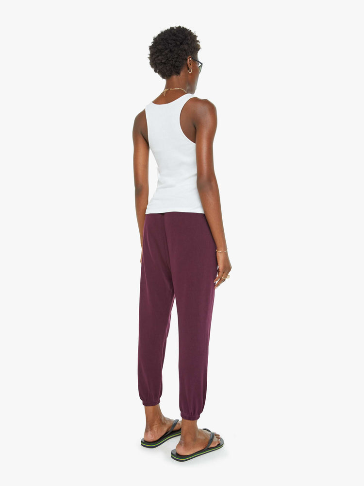 Back view of a woman in an eggplant color sweatpants with a drawstring waistband, elastic hems, a loose, wide leg and the brand's logo in grey at the hip.