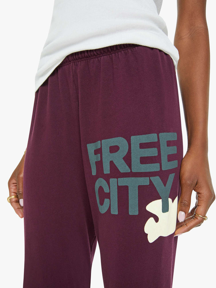 Waist close up view of a woman in an eggplant color sweatpants with a drawstring waistband, elastic hems, a loose, wide leg and the brand's logo in grey at the hip.