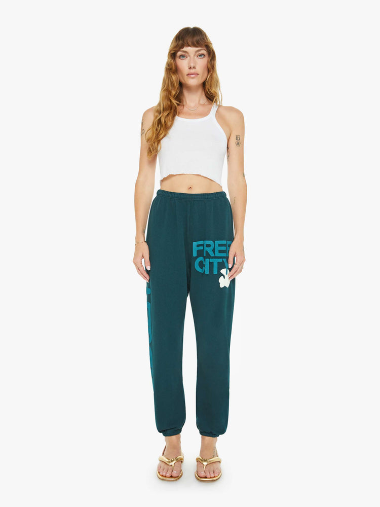 Front view of a woman in sweatpants designed with a drawstring waistband, elastic hems, a loose leg and text on the front and side.