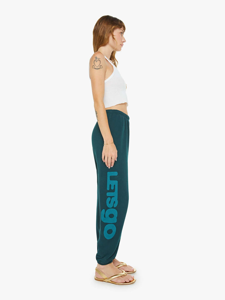 Side view of a woman in sweatpants designed with a drawstring waistband, elastic hems, a loose leg and text on the front and side.