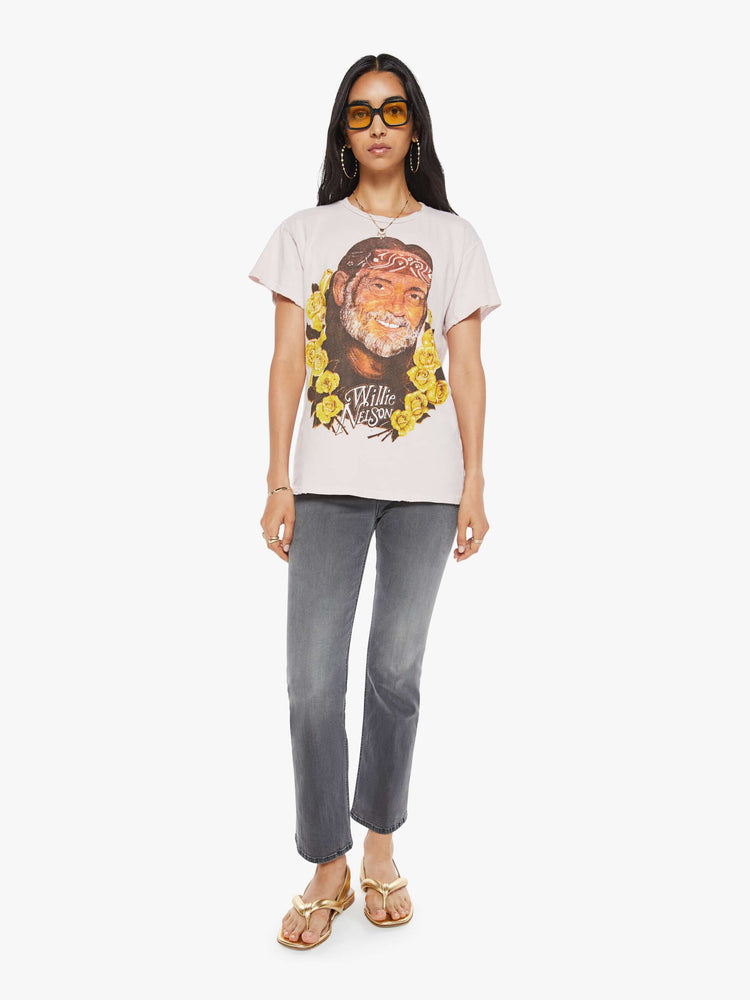 Full body view of a woman in a distressed crewneck tee in faded baby pink, the tee pays homage to Willie Nelson with a graphic portrait on the front.