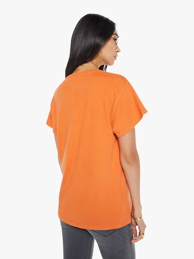 Back view of a woman in a distressed crewneck tee in orange, the tee pays homage to Janis Joplin's 1967 tour with a graphic portrait on the front.