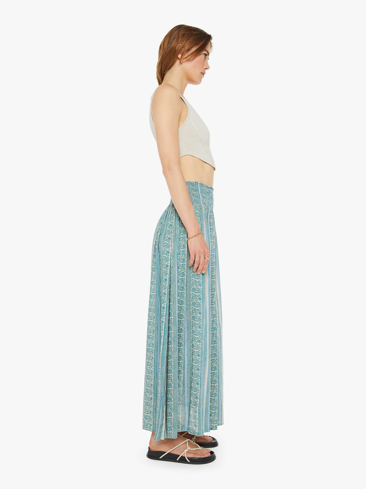 Side view of a woman maxi skirt in a teal stripe pattern, the skirt has a smocked waistband and a loose, flowy fit.