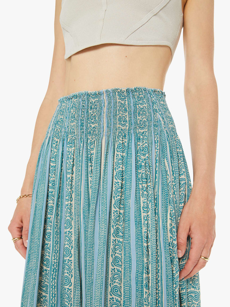 Close up view of a woman maxi skirt in a teal stripe pattern, the skirt has a smocked waistband and a loose, flowy fit.