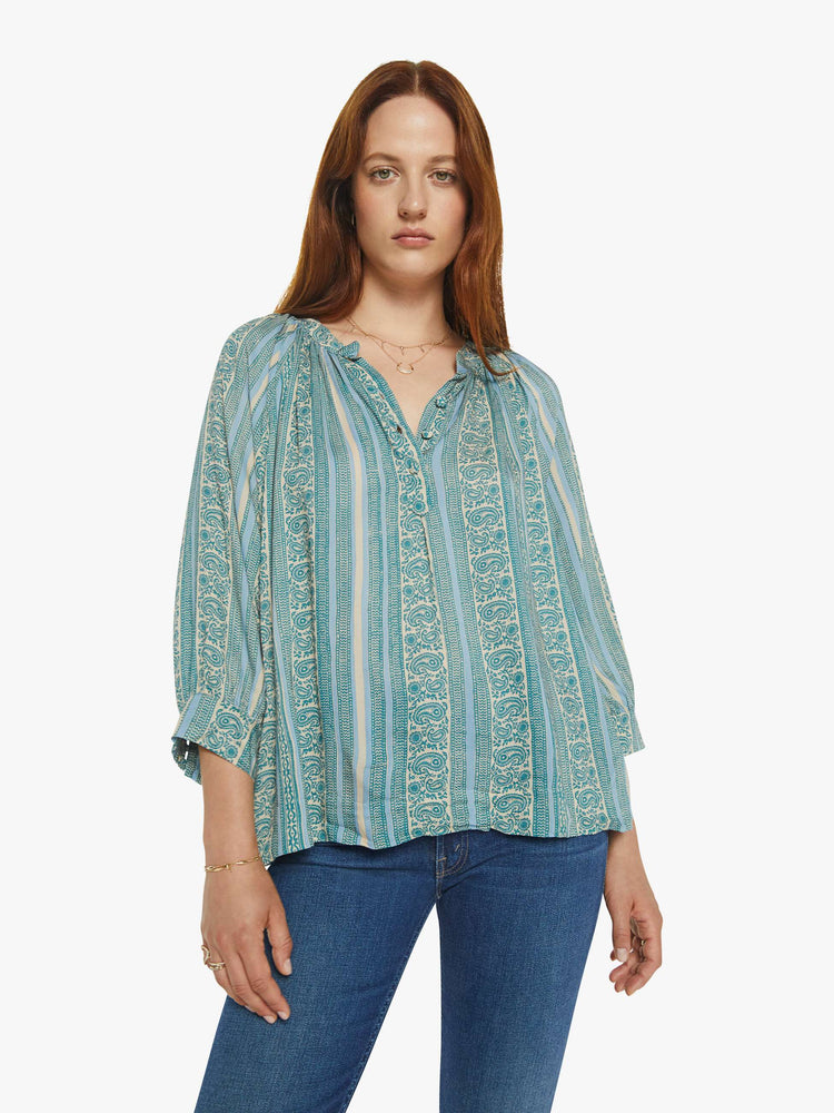 Front view of a woman V-shaped neckline shirt with covered buttons and subtle pleats below the collar emphasizes the loose, flowy feel in a teal stripe pattern.