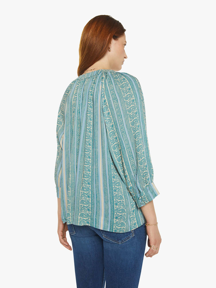 Back view of a woman V-shaped neckline shirt with covered buttons and subtle pleats below the collar emphasizes the loose, flowy feel in a teal stripe pattern.