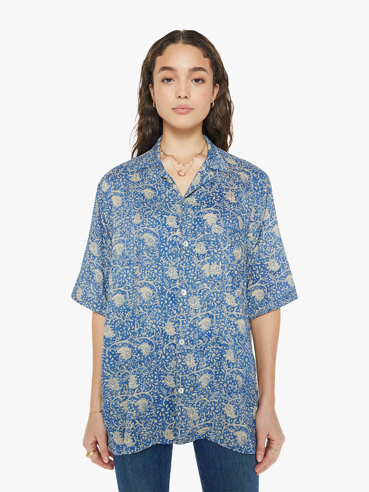 Front view of a woman in a shirt with a designed in a blue floral print, and features a V-neck, drop shoulders, elbow-length sleeves, buttons down the front and a long, thigh-grazing hem.