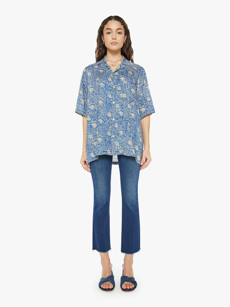 Full body view of a woman in a shirt with a designed in a blue floral print, and features a V-neck, drop shoulders, elbow-length sleeves, buttons down the front and a long, thigh-grazing hem.