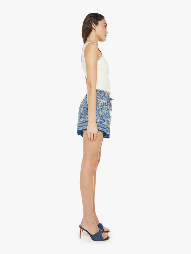 Side view of a woman in floral blue shorts are designed with an elastic high waist, side slit pockets, a slightly curved hem and a loose, flowy fit.