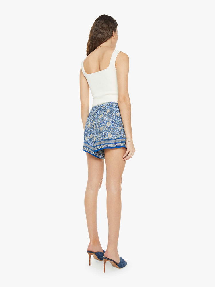 Back view of a woman in floral blue shorts are designed with an elastic high waist, side slit pockets, a slightly curved hem and a loose, flowy fit.