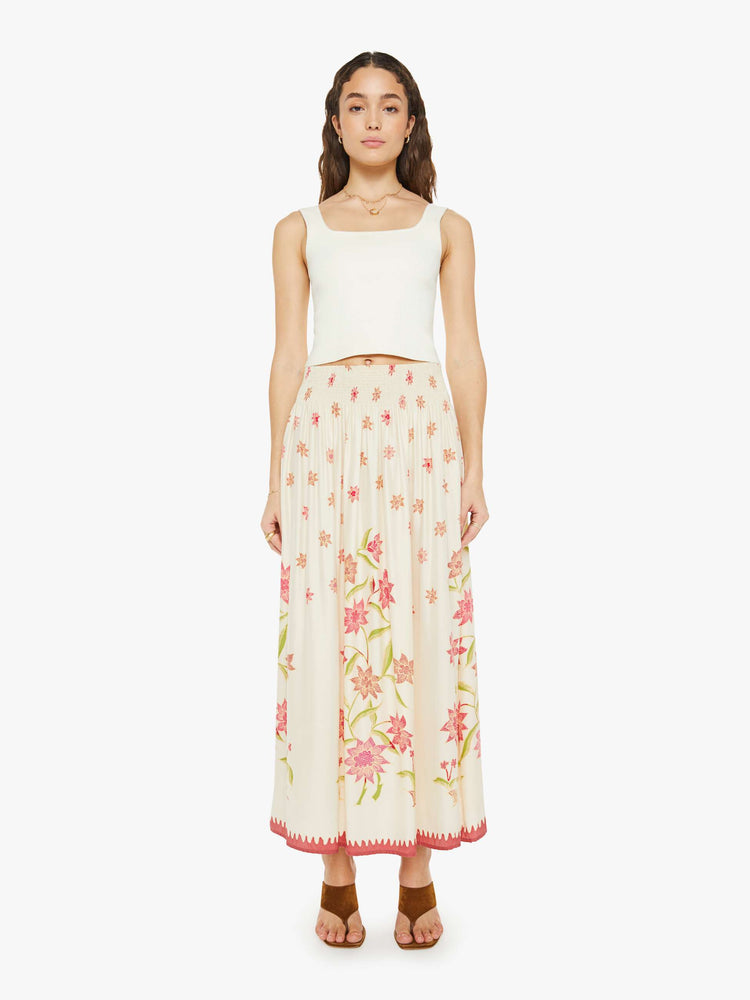 Front view of a woman in a  cream with a pink floral print, the skirt has a smocked waistband and a loose, flowy fit. 