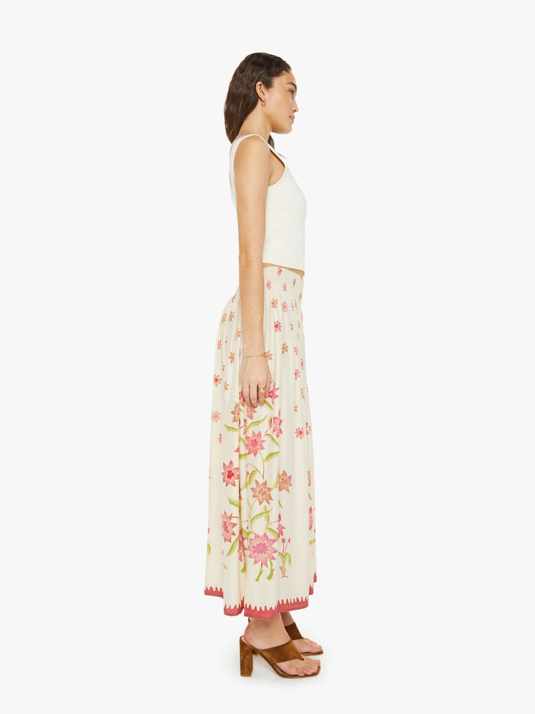 Side view of a woman in a cream with a pink floral print, the skirt has a smocked waistband and a loose, flowy fit.