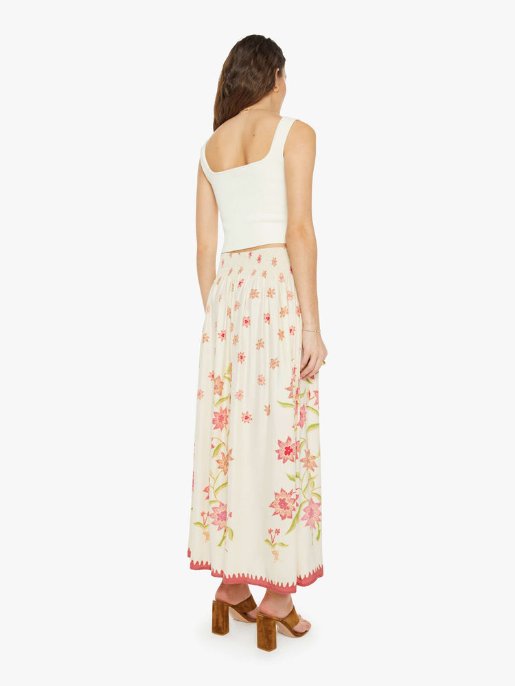 Back view of a woman in a cream with a pink floral print, the skirt has a smocked waistband and a loose, flowy fit.