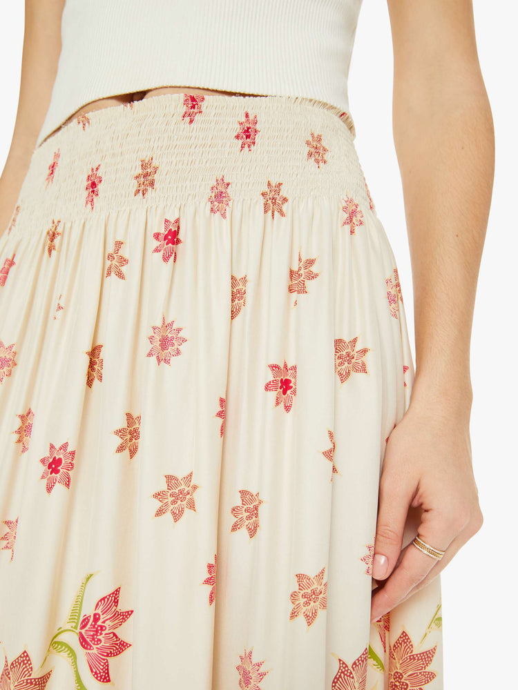 Close up view of a woman in a cream with a pink floral print, the skirt has a smocked waistband and a loose, flowy fit.