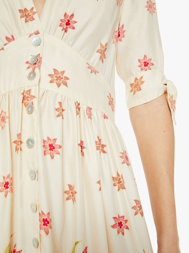 Swatch view of a woman in a cream with a pink floral print midi dress has a deep V-neck, elbow-length sleeves that tie, buttons down the front and ruffled details throughout.